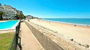 Una playa con piscina, una barrera de hormigón y edificios al fondo.