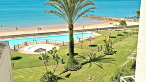 Zona de piscina con palmera, playa y vista despejada del océano.