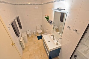 Ein modernes Badezimmer mit einem großen Spiegel, einem Waschbecken, einem Bidet und einer Toilette.