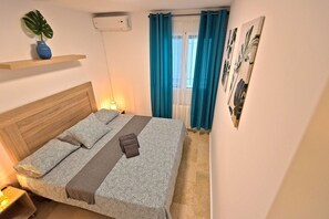 Ein Schlafzimmer mit einem Holz-Kopfteil, einem Bett mit gemusterten Betttextilien, einer Nachttischlampe, einem Blumentopf und einer Wand-Klimaanlage.