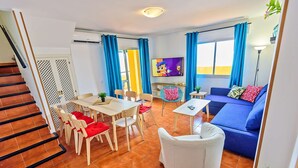 A modern living room with a blue sofa, white armchairs, and a dining table.