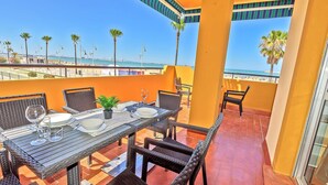 A balcony with a table set for two, overlooking a beach.