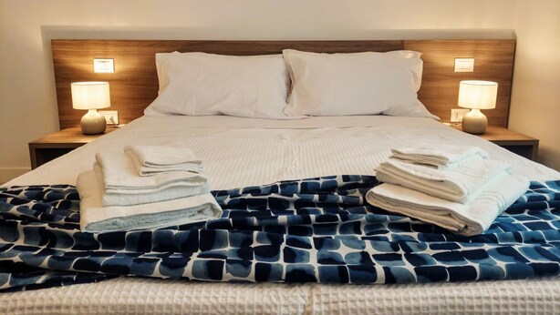 A neatly made bed with white linens, a blue patterned blanket, and two bedside lamps on wooden nightstands. - Brand new renovated apartment "The Dormouse" 10 minutes from the historic center (Firenze)