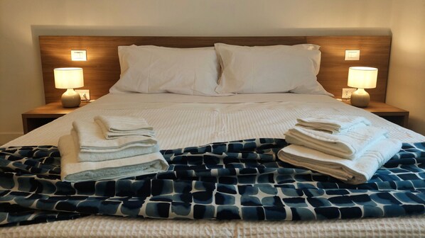 A neatly made bed with white linens, two pillows, and a blue patterned blanket. There are two bedside lamps on wooden nightstands.