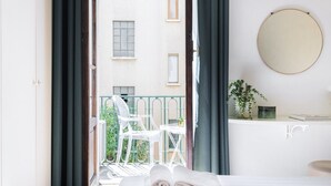 A hotel room with a balcony, a bed, a round mirror, and a small table with a plant.