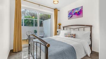 A bedroom with a bed, a window with curtains, a chair, and a painting on the wall.