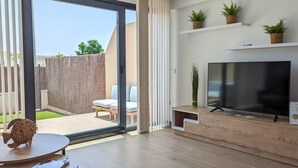 A modern living room with a large TV, wooden furniture, and a sliding glass door leading to a patio. - ASTER relax & spa dúplex (Villajoyosa)