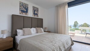 A bedroom with a large bed, two wall-mounted paintings, a nightstand with a lamp, and a view of the outdoors through a large window. - ASTER relax & spa dúplex (Villajoyosa)