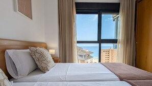 A hotel room with a large bed, a nightstand with a lamp, and a view of the sea through a window. - FLORIDA sea view apartment (Benidorm)