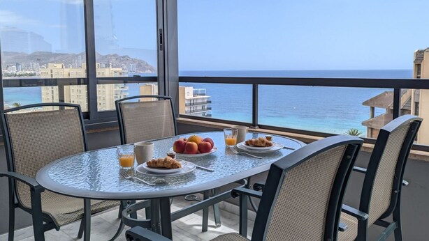 A balcony table with breakfast items, wicker chairs, and a view of the sea and cityscape. - FLORIDA sea view apartment (Benidorm)