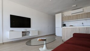 A modern living room with a glass coffee table, a red sofa, a flat-screen TV mounted on the wall, and a kitchen area with wooden cabinets and a white countertop. - ESMERALDA sea front apartment (Benidorm)