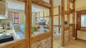 Un interior rústico con vigas de madera a la vista, un comedor con mesa y sillas, una cocina con estufa y alacenas, y un ventanal con vistas.