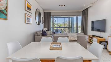 A modern living room with a dining table, white chairs, a sofa, and a TV.