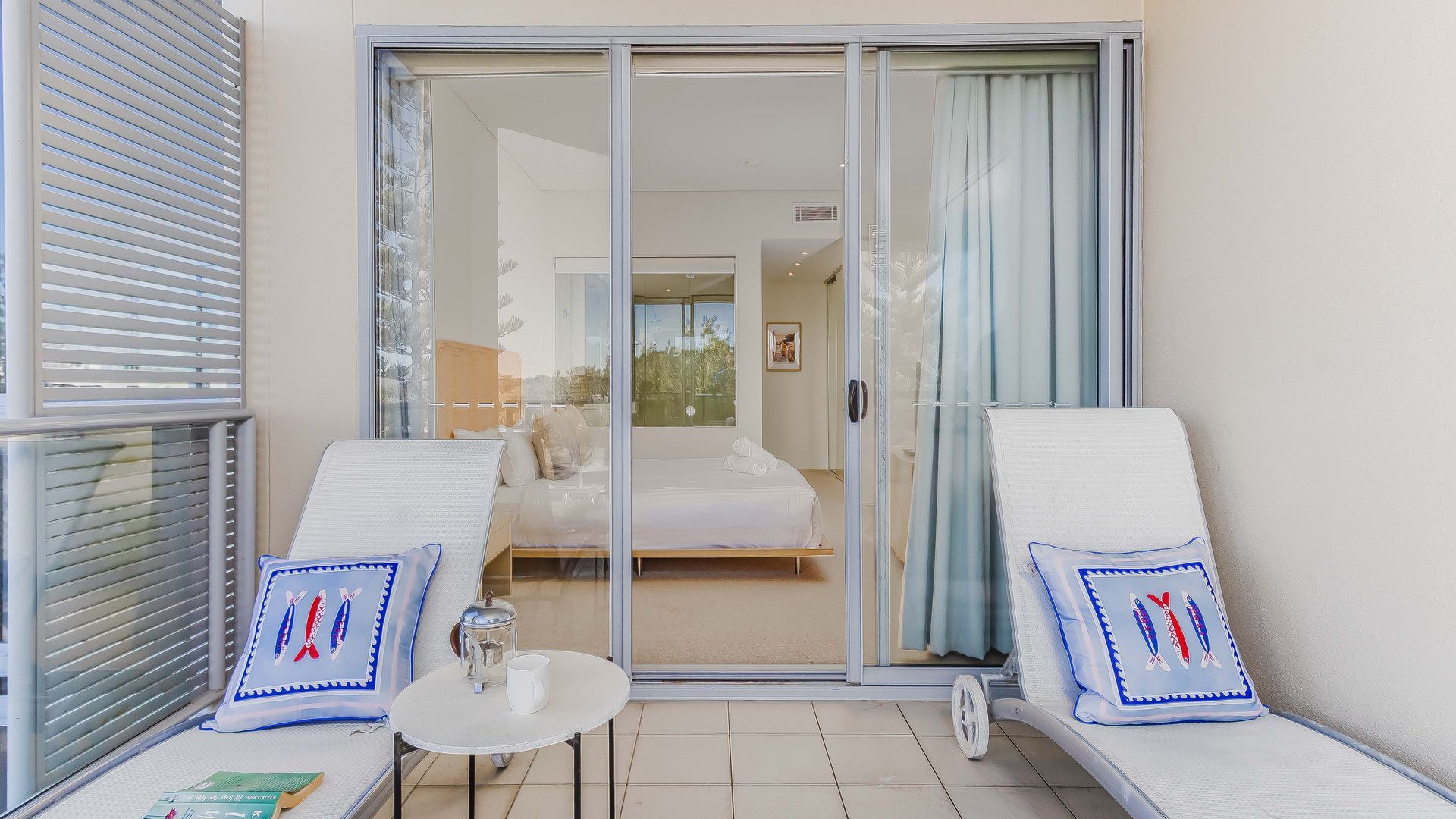 A balcony with two lounge chairs, a small table, and a glass door leading to a bedroom.