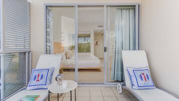 A balcony with two lounge chairs, a small table, and a glass door leading to a bedroom.