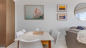Ein Essbereich mit einem weißen Tisch, Stühlen und einem gewebten Korb. An der Wand befinden sich gerahmte Bilder.