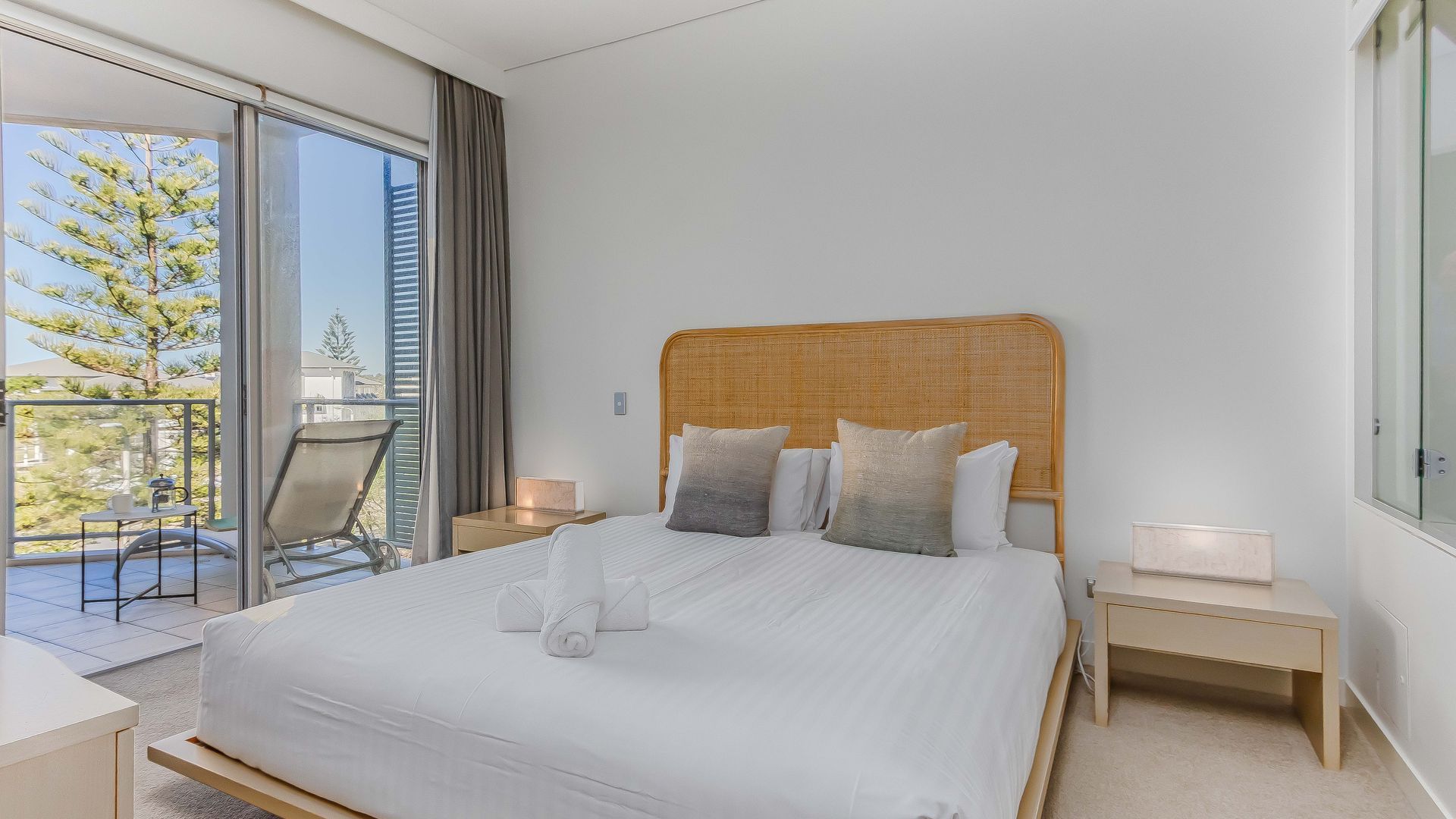 A hotel room with a large bed, a balcony with a chair, and a view of trees.