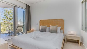 A hotel room with a large bed, a balcony with a chair, and a view of trees.