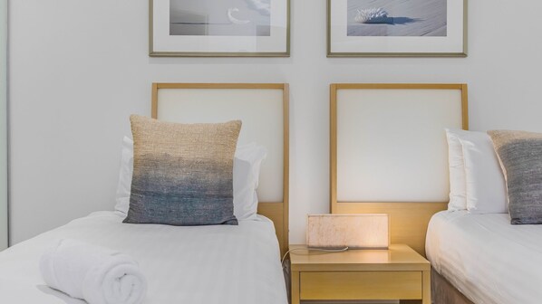 A hotel room with two beds, each with a pillow and a nightstand with a lamp.