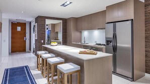 Een moderne keuken met een centraal eiland, barkrukken, een koelkast en een fornuis.