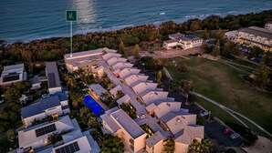 An aerial view of a modern resort with multiple buildings, a swimming pool, and a view of the ocean.