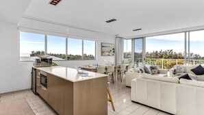 A modern kitchen with a central island, dining area with a sofa and chairs, large windows with a view, and a minimalist design.