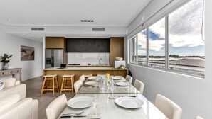 A modern kitchen with a central island, bar stools, and a dining area with a glass table set for six.