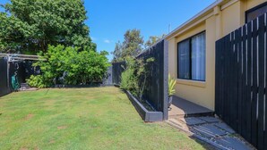A backyard with a lawn, a wooden fence, and a house with a window.