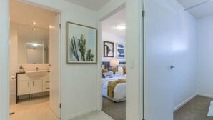 A hotel room with a bathroom, a bed, and a painting on the wall. - Drift Pool View 21 - Elegant Apartment with Spectacular Lagoon Pool and Tropical Garden Views (Casuarina)