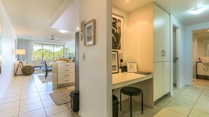 A modern kitchen with a dining area, a large window, and a ceiling fan. - Drift Pool View 21 - Elegant Apartment with Spectacular Lagoon Pool and Tropical Garden Views (Casuarina)