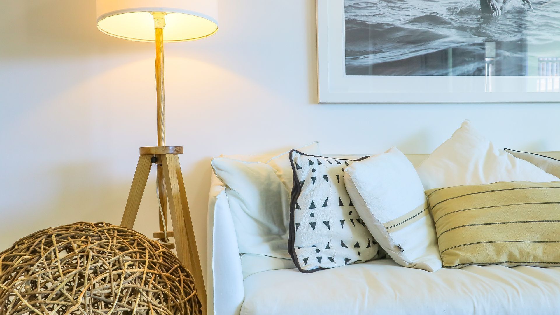 A room with a white sofa, a floor lamp, and a framed picture on the wall.