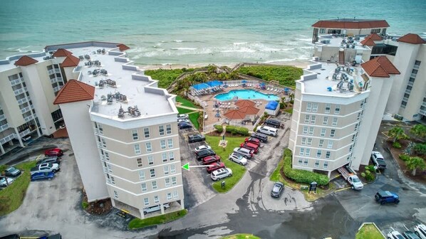 A high-rise hotel with a rooftop pool, multiple balconies, and a parking area.
