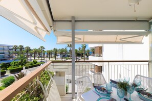Ein Balkon mit Esstisch, Sitzgelegenheiten im Freien und Blick auf Palmen und Gebäude.