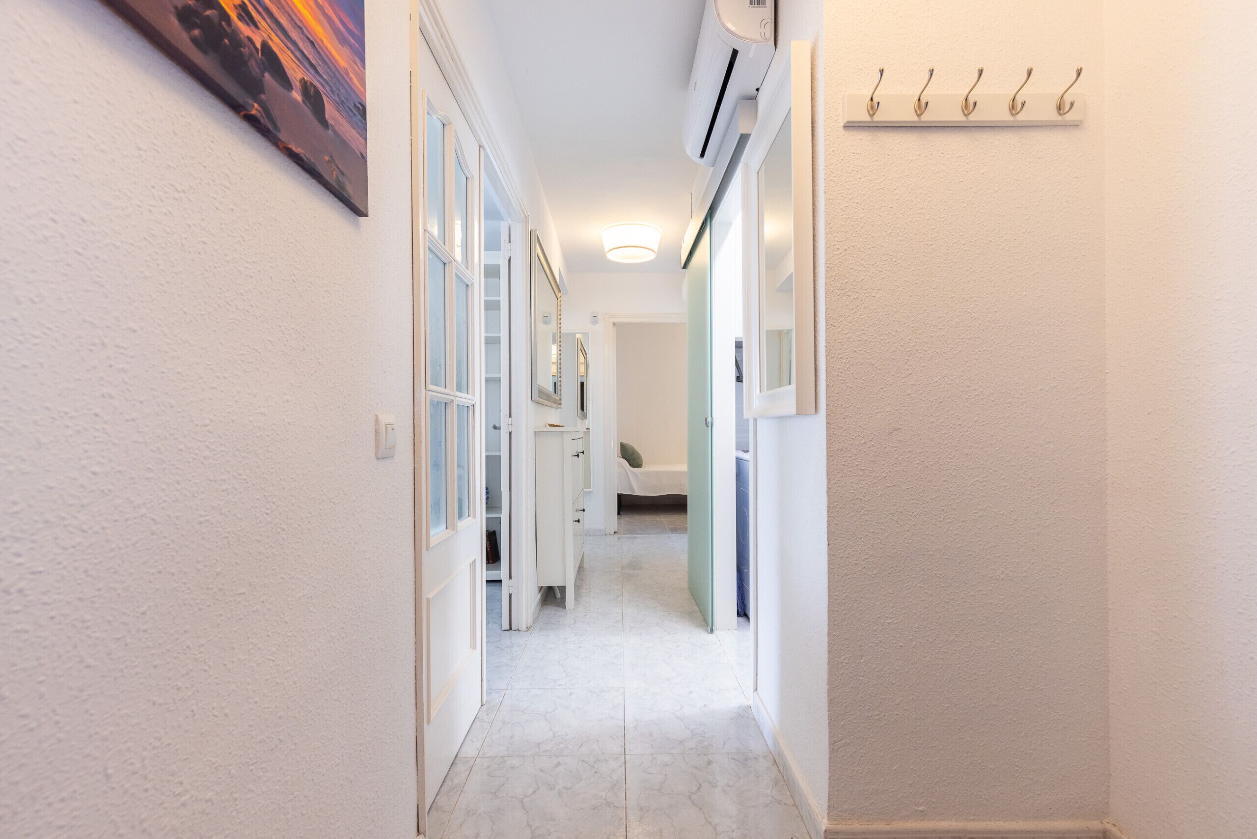 A hallway with a white floor, a ceiling light, and a wall-mounted air conditioner.