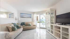 Una sala de estar con un sofá color beige, un televisor y un aparador de vidrio.