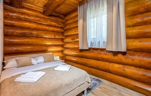 A log cabin bedroom with a bed, pillows, and a window with curtains. - Luxurious home in Fuzine with sauna (Fuzine)