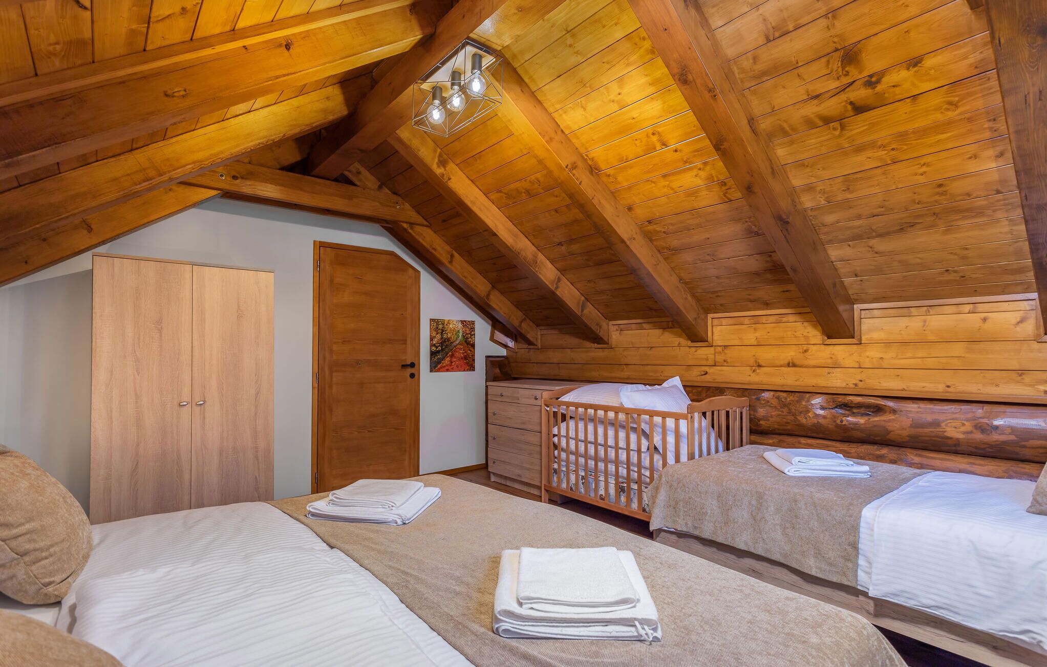 Une chambre mansardée chaleureuse avec des poutres en bois, un lit superposé, un berceau et une armoire.