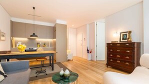 Ett modernt vardagsrum med en soffa, ett soffbord, ett trägolv och en köksdel med ett matbord och en hängande lampa.