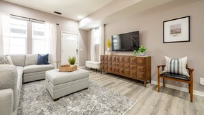 A living room with a sofa, ottoman, wooden cabinet, and a chair. - Indy Elegance | Minutes to Downtown | Free Parking (Indianapolis)