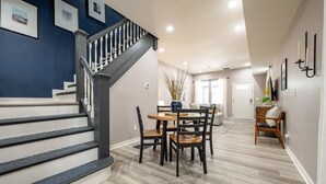A modern interior with a staircase, dining area, and a hallway leading to a door. - Indy Elegance | Minutes to Downtown | Free Parking (Indianapolis)