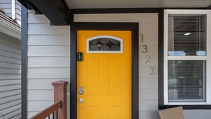 A yellow door with a 'Hello' mat, a number display, and a wicker chair on the porch. - Indy Elegance | Minutes to Downtown | Free Parking (Indianapolis)