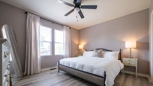 A bedroom with a bed, two bedside tables, a ceiling fan, and a window with curtains. - Indy Elegance | Minutes to Downtown | Free Parking (Indianapolis)