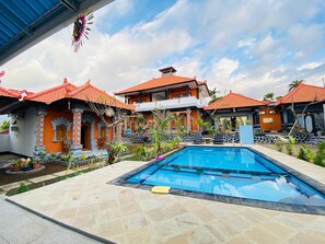 A swimming pool area with tiled flooring, surrounded by a poolside lounge with chairs and a small table. - Villa Jepun (Buleleng)