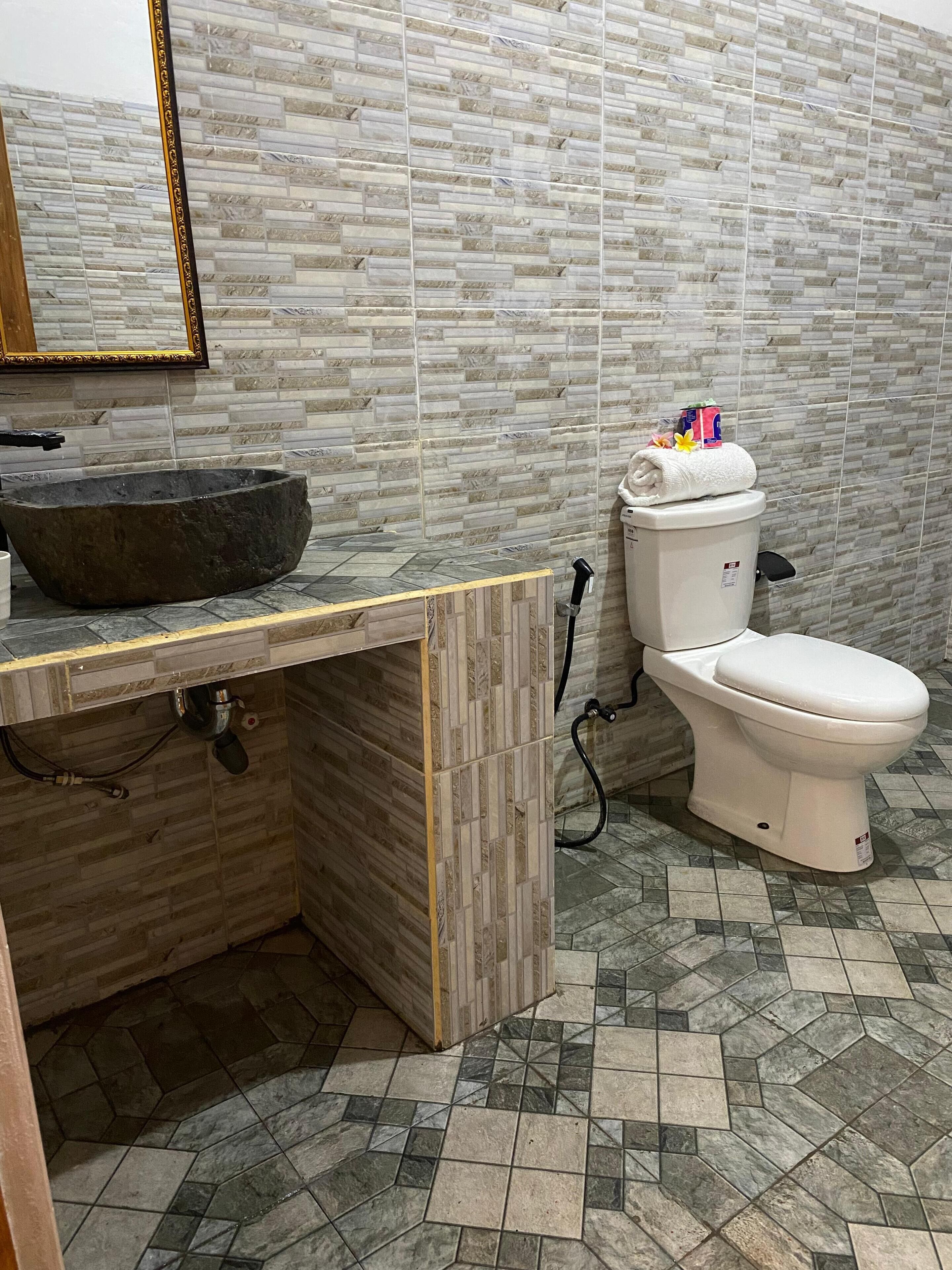 A bathroom with a stone sink, toilet, and tiled floor.