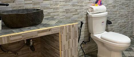 A bathroom with a stone sink, toilet, and tiled floor.