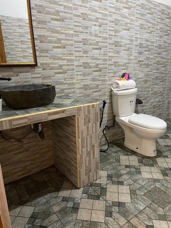 A bathroom with a stone sink, toilet, and tiled floor. - Villa Jepun (Buleleng)