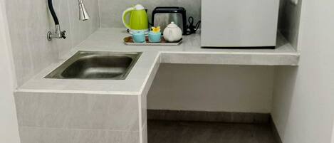 A compact kitchen with a sink, a kettle, a toaster, and a refrigerator.