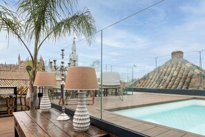 A rooftop pool area with a wooden table, two lamps, and a view of a historic building with a tower. - Casa del Contratador by Época Suites (Seville)