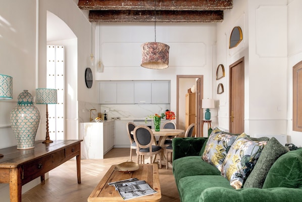 A living room with a green sofa, wooden coffee table, and a dining area with a white table and chairs. - Casa del Contratador by Época Suites (Seville)