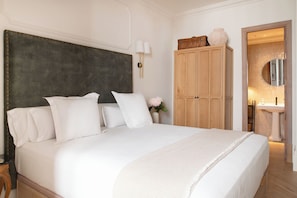 A large bed with a dark headboard, white bedding, and a herringbone-patterned throw. A wooden wardrobe and a mirror are visible in the background. - Casa del Contratador by Época Suites (Seville)
